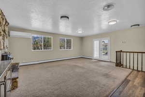 Unfurnished living room with a textured ceiling, french doors, healthy amount of natural light, a baseboard heating unit, and carpet