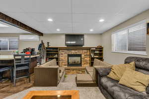 Living area featuring a stone fireplace, healthy amount of natural light, a drop ceiling, and recessed lighting