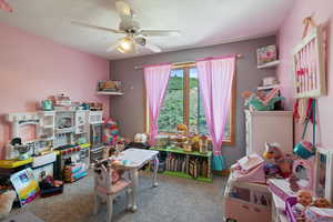 Playroom with a textured ceiling, light colored carpet, and a ceiling fan