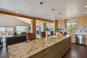 Kitchen with open floor plan, beam ceiling, dark wood finished floors, light stone countertops, and stainless steel dishwasher