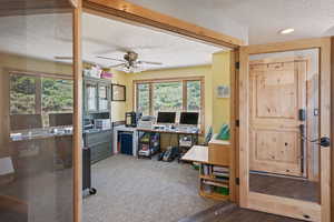 Office space with a textured ceiling, ceiling fan, and light colored carpet