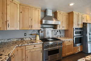 Kitchen featuring light wood finish cabinets, stainless steel appliances, light stone counters, and a textured ceiling
