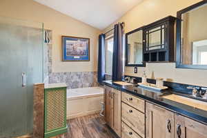 Full bath with double vanity, vaulted ceiling, a garden tub, dark wood-style flooring, and a shower stall