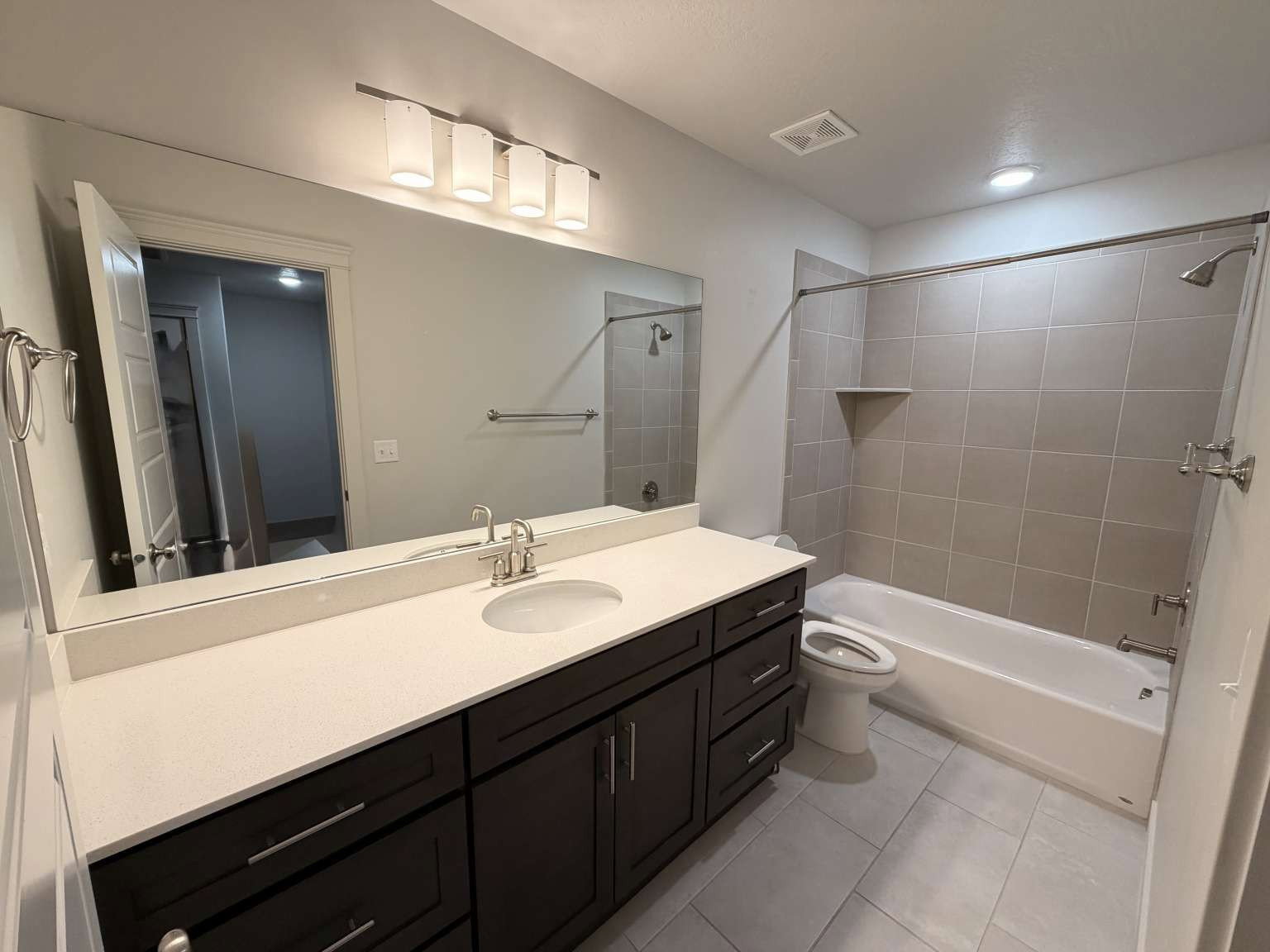 Bathroom featuring a spacious vanity with dark wood cabinetry, a light-toned countertop, and a large mirror