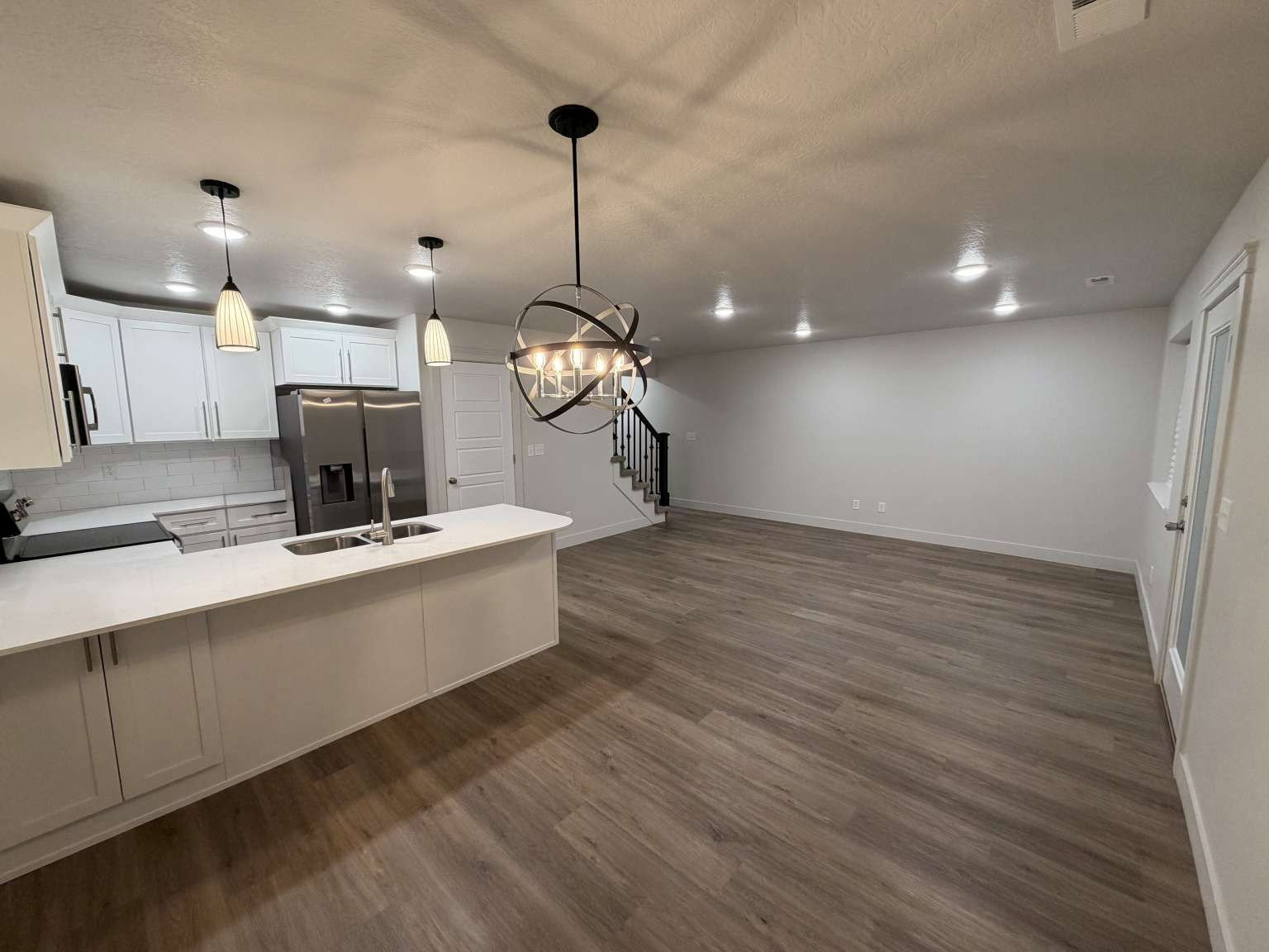 Open-concept living space featuring a kitchen island with sink, stainless steel appliances, white cabinetry, and wood-finish flooring