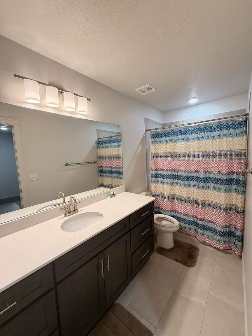 Single vanity featuring a white oval sink set in a light-toned countertop, dark wood-finish cabinetry with brushed nickel pulls, and a large wall-mounted mirror