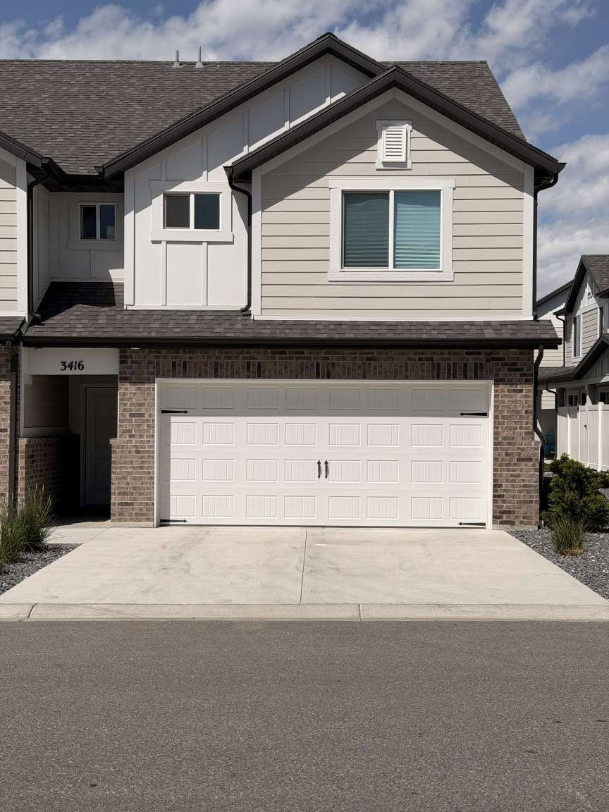 Contemporary townhouse exterior featuring a white paneled garage door, a concrete driveway, and a brick facade