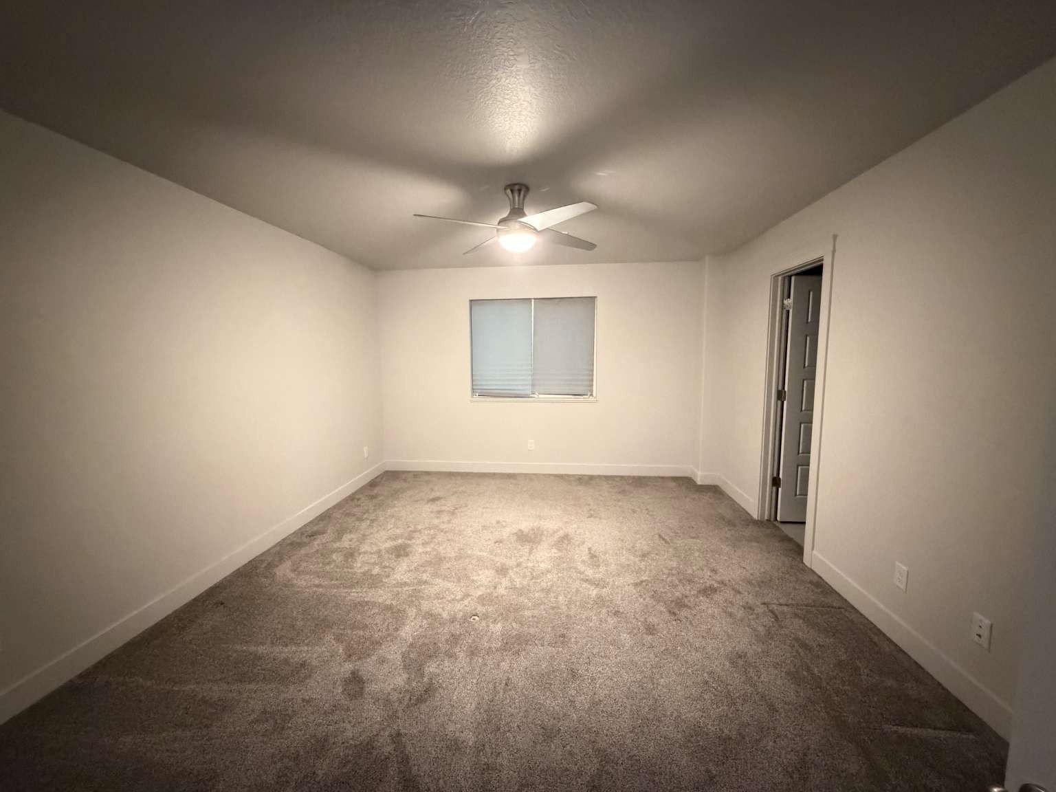 Spacious room with plush gray carpeting, neutral wall paint, and a ceiling fan with integrated lighting