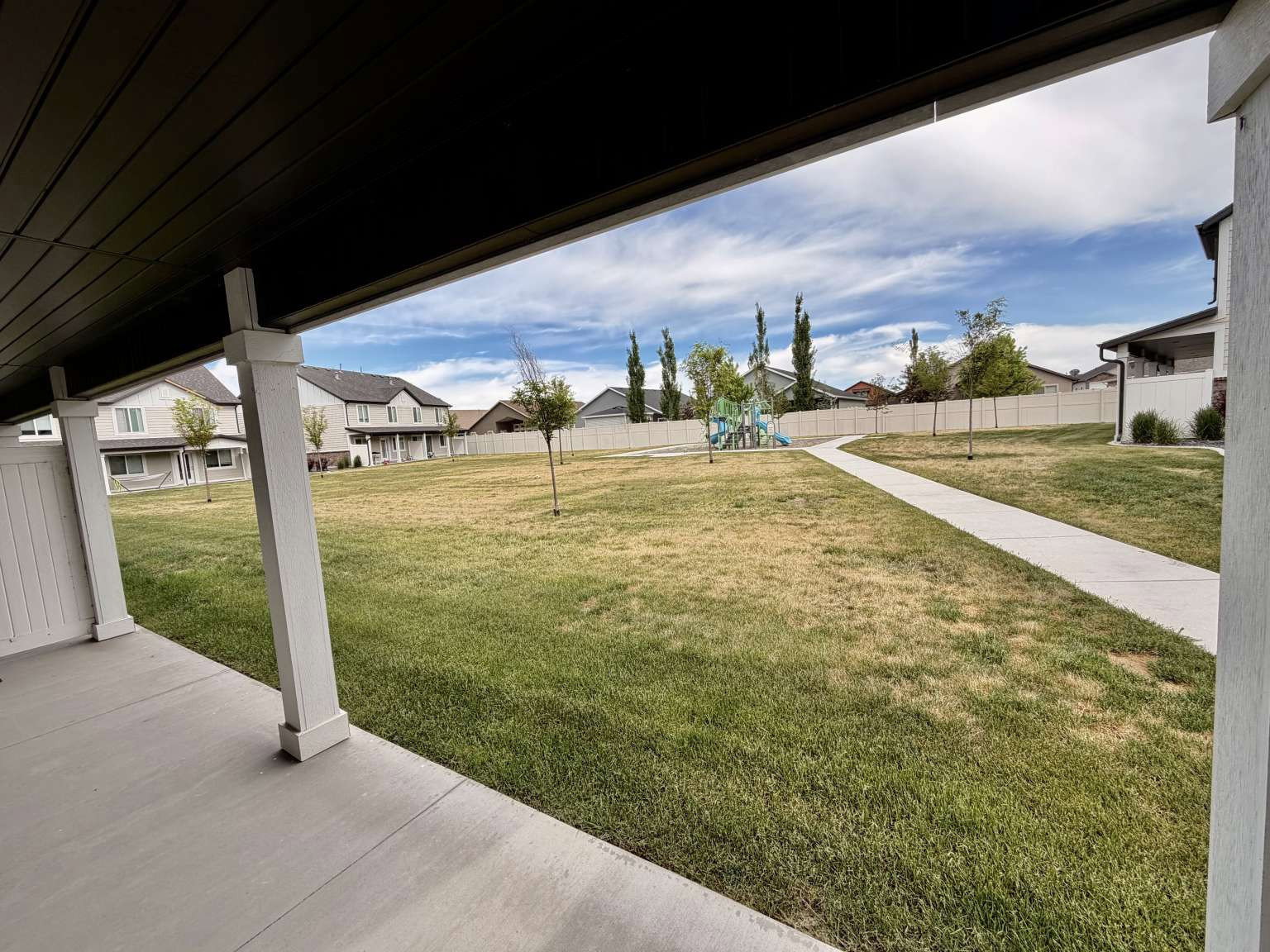 Covered patio with white support columns, overlooking a green space with a paved pathway