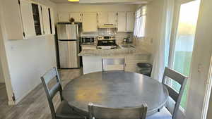 Kitchen featuring stainless steel appliances, light wood-type flooring, tasteful backsplash, and white cabinetry