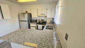 Kitchen with white cabinets, decorative backsplash, stainless steel appliances, a peninsula, and light stone countertops