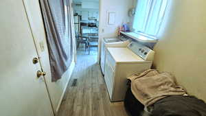 Laundry room featuring light wood-style floors, separate washer and dryer, a textured wall, and electric panel