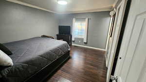 Bedroom with dark wood finished floors, ornamental molding, and a textured wall