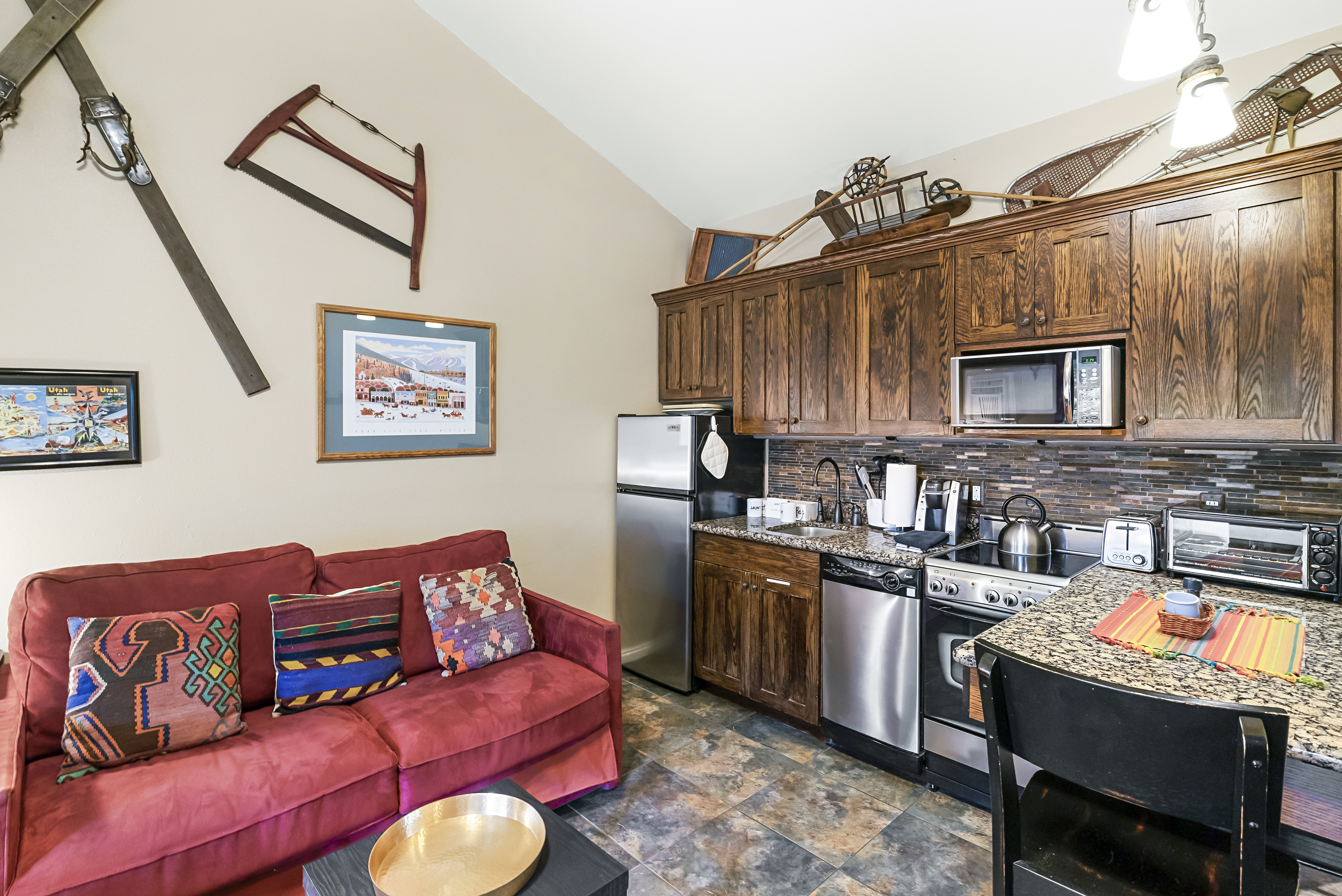 Kitchen featuring stainless steel appliances, dark wood finish cabinetry, stone finish floors, light stone countertops, and open floor plan