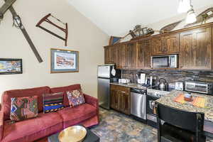 Kitchen featuring stainless steel appliances, dark wood finish cabinetry, stone finish floors, light stone countertops, and open floor plan