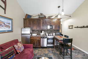 Kitchen with freestanding refrigerator, dark wood finish cabinets, lofted ceiling, stone finish flooring, and electric range