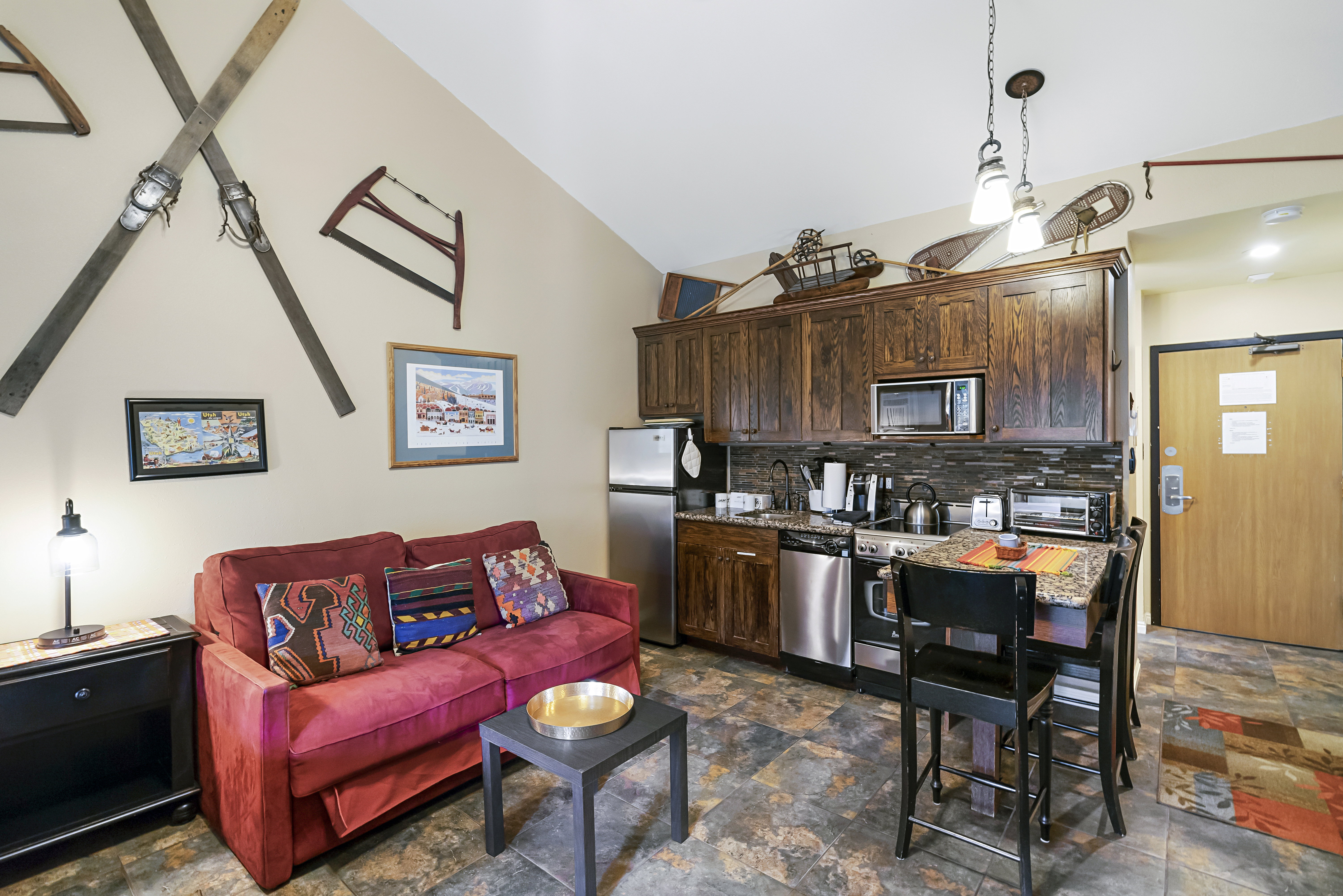 Kitchen featuring dark wood finish cabinets, vaulted ceiling, stainless steel appliances, dark stone finish flooring, and backsplash