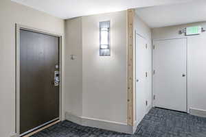 Entrance foyer with baseboards and dark colored carpet
