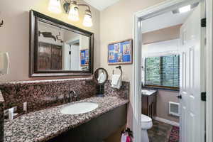Bathroom with vanity, tasteful backsplash, dark stone finish floors, and heating unit