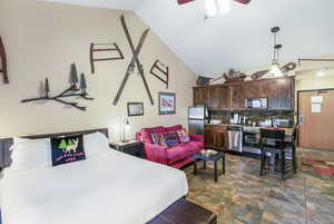 Bedroom with vaulted ceiling, stone finish flooring, a ceiling fan, and freestanding refrigerator