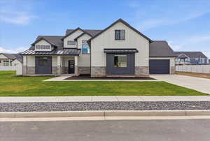 Modern farmhouse style home with stone siding, a standing seam roof, concrete driveway, an attached garage, and a porch