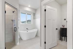 Bathroom with wainscoting, a stall shower, a soaking tub, a decorative wall, and light tile patterned floors