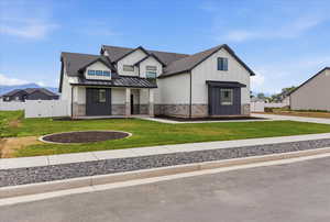Modern farmhouse style home featuring a standing seam roof, a porch, a gate, stone siding, and board and batten siding