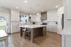 Two tone kitchen with a breakfast bar, open shelves, a center island, light wood finished floors, and stainless steel appliances