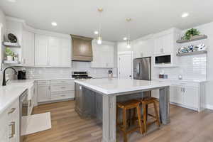 Kitchen featuring open shelves, stainless steel appliances, two tone cabinets, light wood-style flooring, and a kitchen island