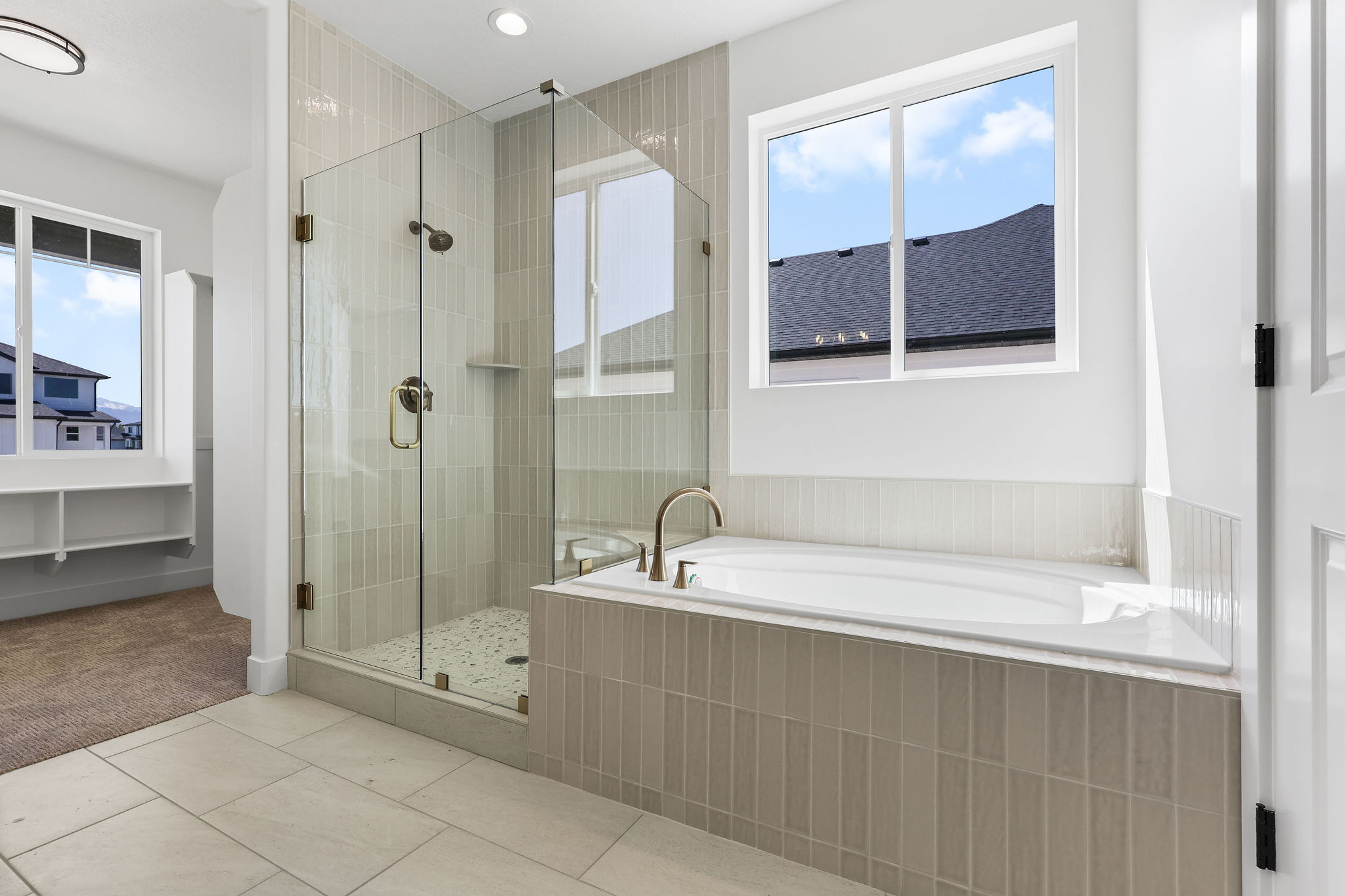 Spacious bathroom featuring a built-in soaking tub with a tiled surround, a glass-enclosed shower with vertical tile accents and pebble flooring, and light-toned floor tiling