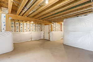 Unfinished basement with concrete flooring and exposed wood ceiling joists