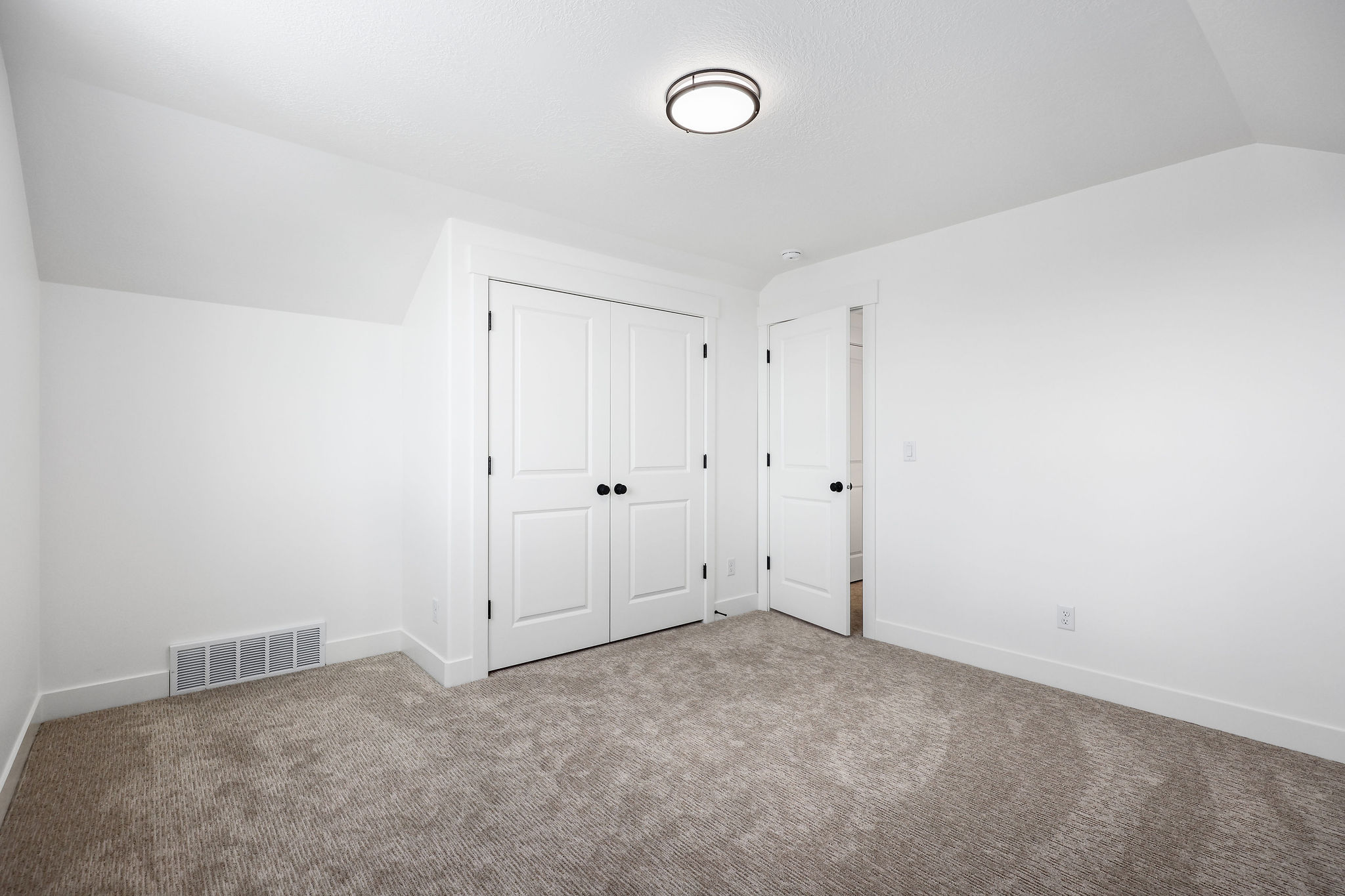 White walls and neutral carpeting define this interior space, featuring a double-door closet with black hardware