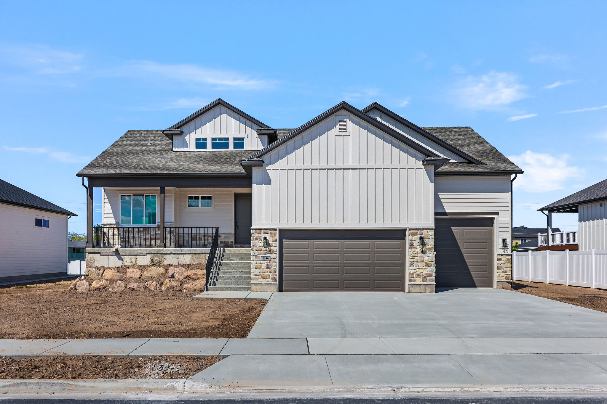 Modern Farmhouse exterior featuring a covered front porch, a two-car garage, stone accents, and vertical siding