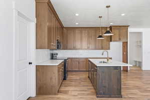 Kitchen featuring wood-finish cabinetry, white countertops, subway tile backsplash, and stainless steel sink with a brass faucet