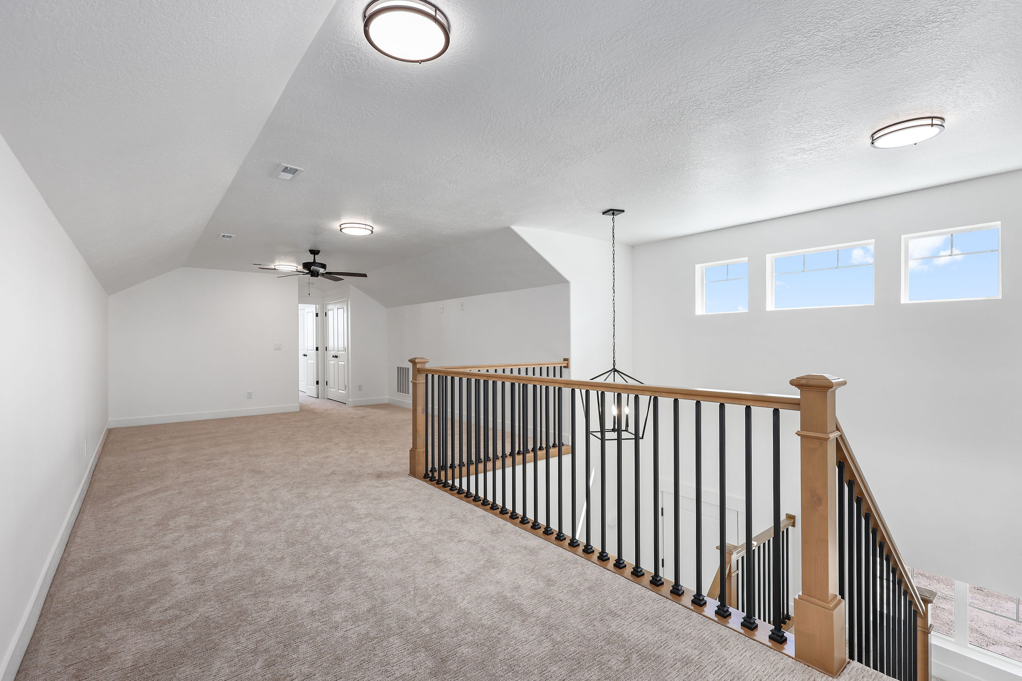 Spacious loft area featuring light-toned carpeting, a black wrought iron and natural wood banister, and three transom windows