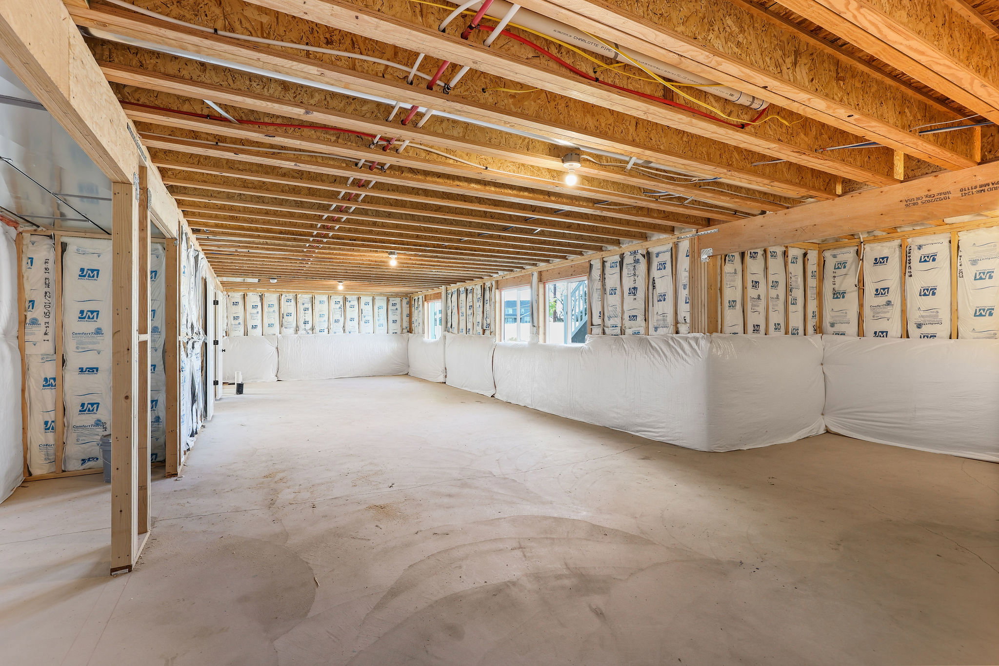 Unfinished basement space featuring exposed wood joists and subflooring, framed walls with insulation, concrete flooring, and multiple light fixtures
