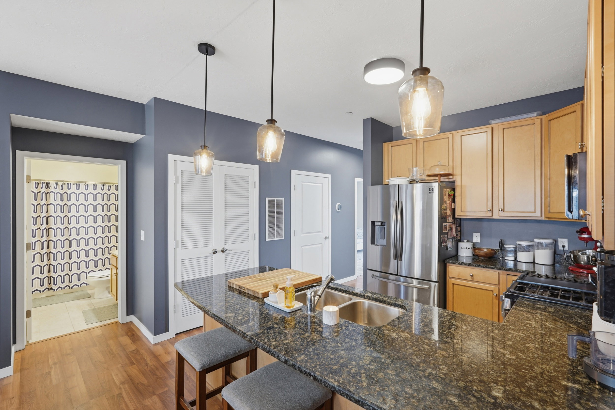 Kitchen featuring a peninsula, a kitchen bar, pendant lighting, dark stone countertops, and stainless steel fridge