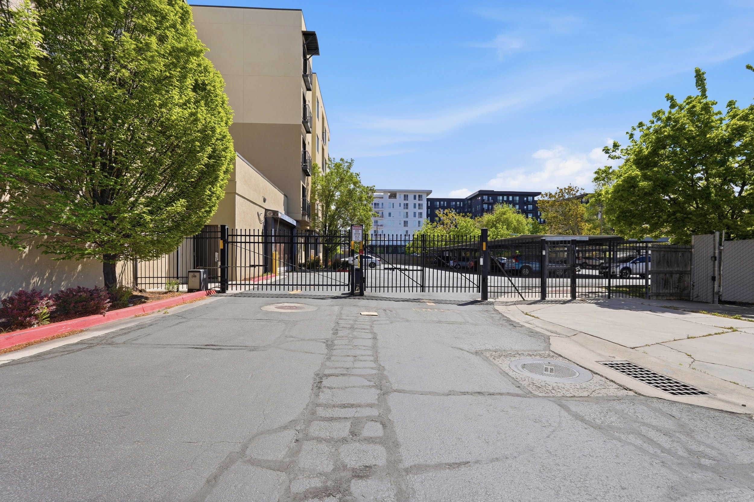 View of asphalt street with a gate, a gated entry, curbs, and sidewalks