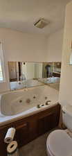 Bathroom with healthy amount of natural light, a textured ceiling, and a tub with jets