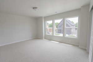 Bright room featuring three large windows, neutral wall paint, light-toned carpeting, and a flush-mount ceiling light fixture