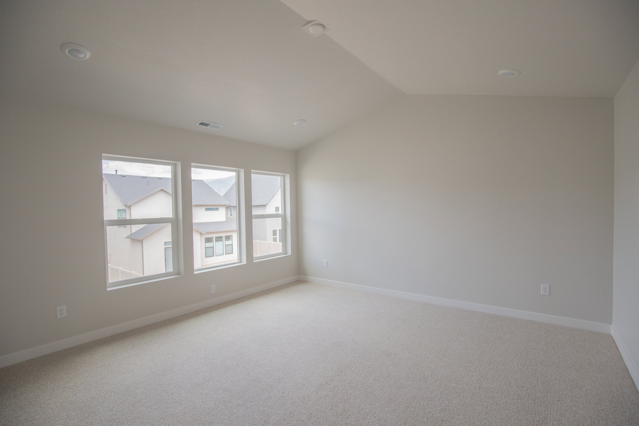 Spacious room featuring three large windows, recessed ceiling lighting, light-colored carpeting, and painted walls with white trim