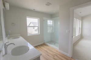 Bathroom featuring a double vanity with undermount sinks and chrome fixtures, a glass-enclosed shower, wood-finish flooring, and a single window