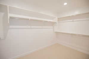 Walk-in closet featuring built-in shelving, chrome hanging rods, recessed ceiling lighting, and neutral carpeting