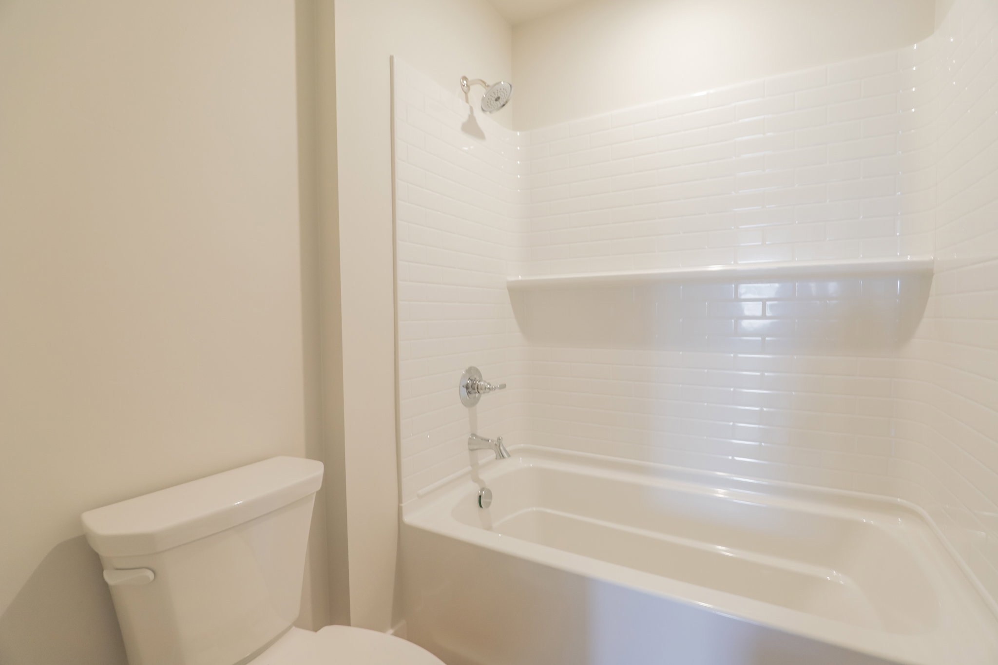White subway tile shower surround with integrated shelving and chrome fixtures