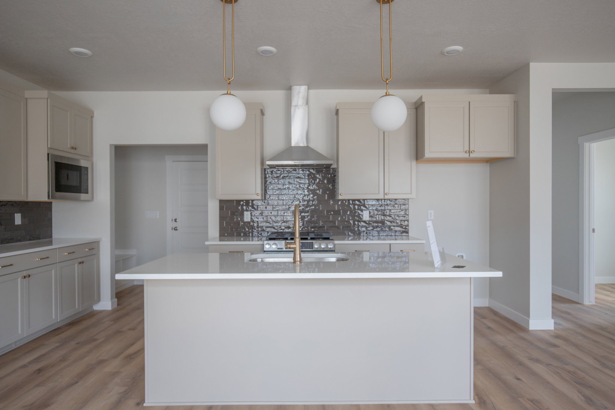 Contemporary kitchen featuring a large central island with a quartz countertop, gold-finish pendant lighting, light gray cabinetry, a stainless steel microwave, and a textured tile backsplash