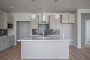 Contemporary kitchen featuring a large central island with a quartz countertop, gold-finish pendant lighting, light gray cabinetry, a stainless steel microwave, and a textured tile backsplash