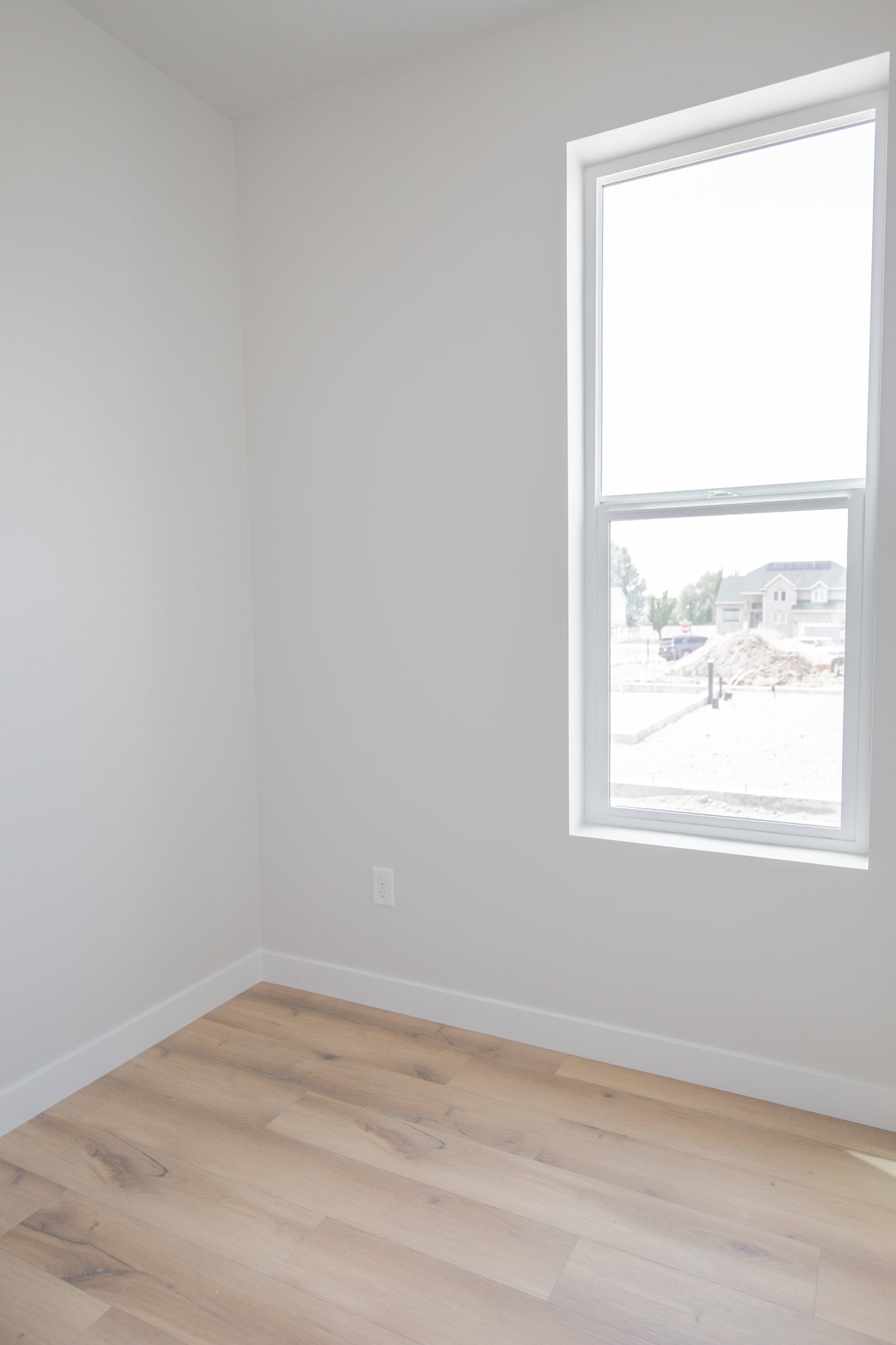 Bright room featuring a large vertical window, light wood-finish flooring, white baseboards, and neutral wall tones