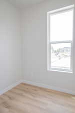 Bright room featuring a large vertical window, light wood-finish flooring, white baseboards, and neutral wall tones