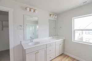 Dual vanity featuring white countertops, undermount sinks, and light-toned cabinetry with gold-toned hardware