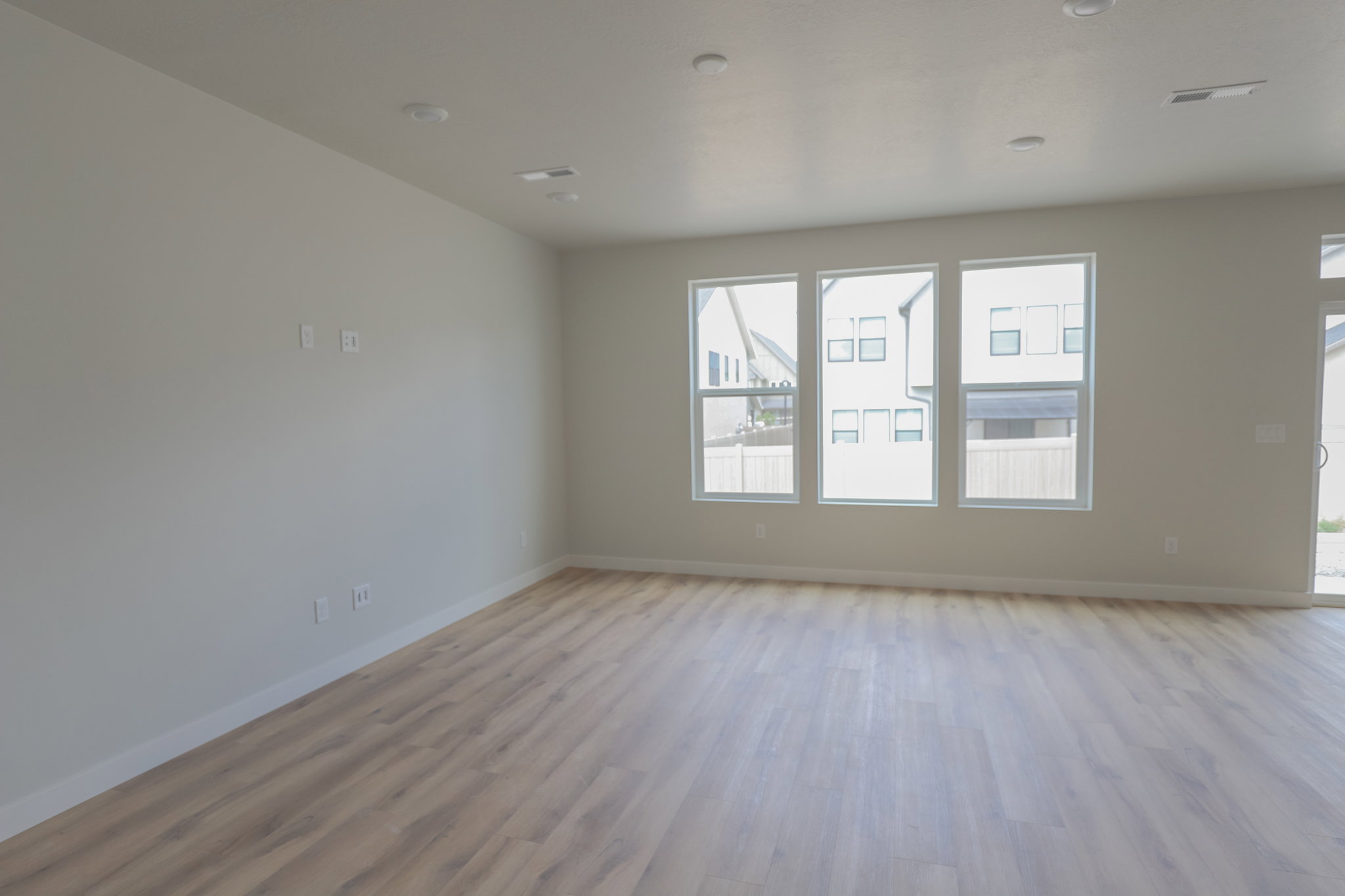 Spacious interior room featuring wood-finish flooring, recessed lighting, and multiple windows with white frames